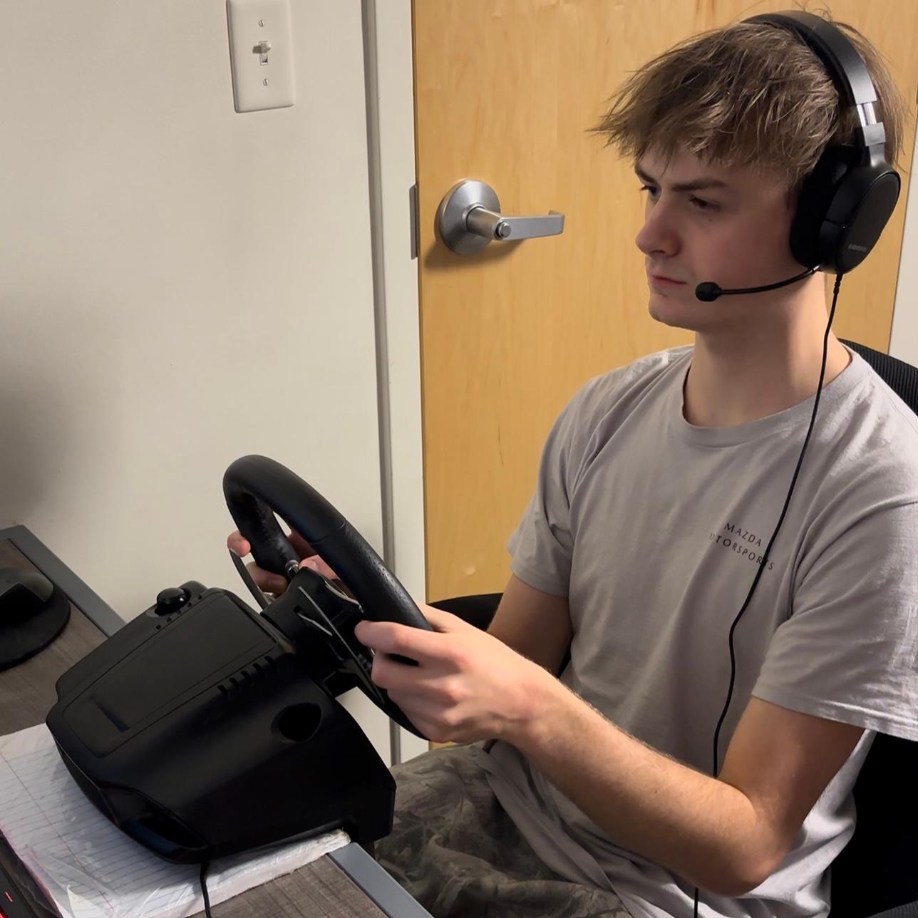 Desk-mounted Logitech G27 with corresponding pedals, operated from an office chair. Single ASUS TUF 32" monitor.